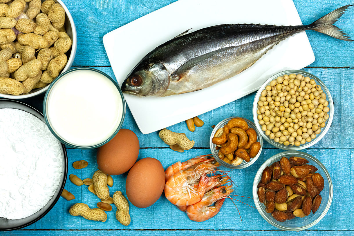 Major food allergens include milk, eggs, peanuts, fish, shellfish, wheat, soybeans and tree nuts on blue rustic wooden table, top view.