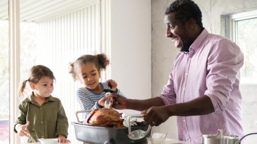 A father bastes a turkey on a counter with help from two young daughters.