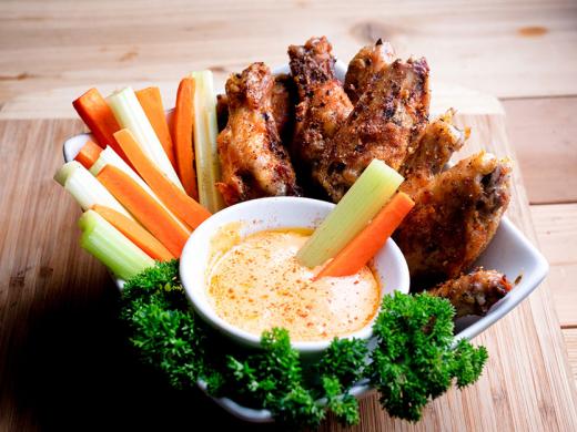 A dish with celery, carrot sticks, and chicken wings and  a bowl of buffalo sauce.