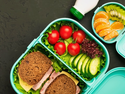 Packed school lunch of ham sandwich, fruit, and yogurt.